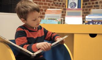 Enfant qui lit un livre devant le meuble d'un espace Édition Jeunesse Accessible Enfant qui lit un livre devant le meuble d'un espace Édition Jeunesse Accessible
